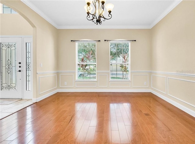 108 Whispering Pines Way, Davenport, FL 33837 - foyer featuring light wood-type flooring, a chandelier, arched walkways, ornamental molding, and a wainscoted wall