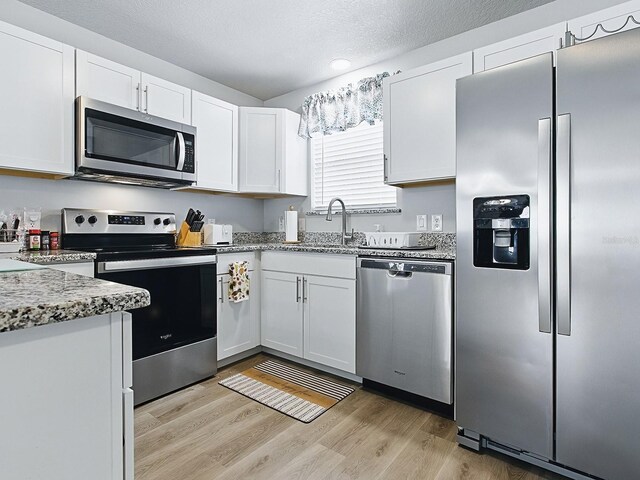 1722 Moreno Pl, The Villages, FL 32159 - kitchen with stainless steel appliances, white cabinetry, light wood-style flooring, a sink, and light stone countertops