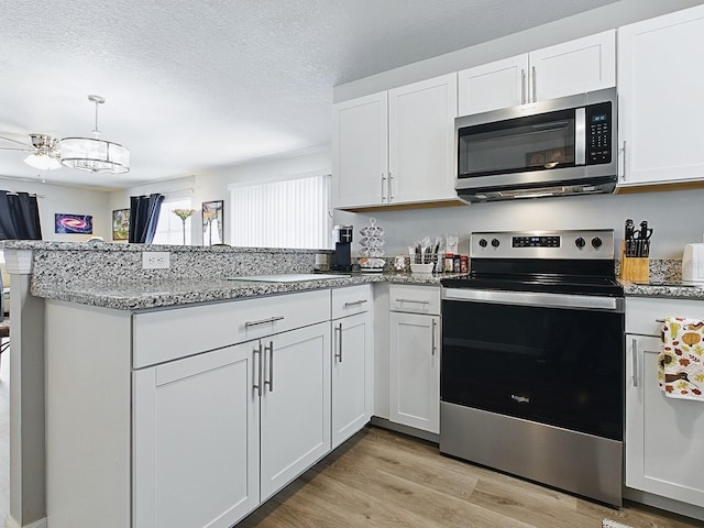 1722 Moreno Pl, The Villages, FL 32159 - kitchen featuring appliances with stainless steel finishes, a peninsula, white cabinets, light stone countertops, and a textured ceiling