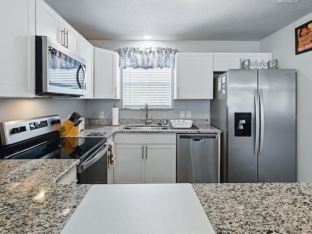 1722 Moreno Pl, The Villages, FL 32159 - kitchen featuring appliances with stainless steel finishes, a sink, white cabinets, a textured ceiling, and light stone counters