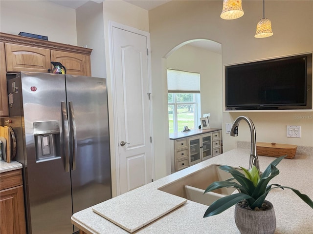 kitchen featuring stainless steel refrigerator with ice dispenser, arched walkways, a sink, light countertops, and hanging light fixtures