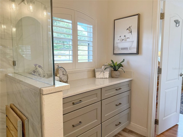 bathroom view of a shower with door, vanity, and wood finished floors