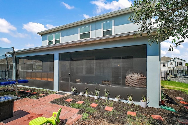 1155 Dora Parc Ln, Mount Dora, FL 32757 - rear view of house featuring a sunroom, a trampoline, a patio area, stucco siding, and a fire pit