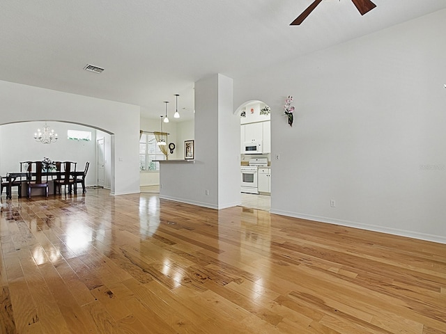 living area featuring arched walkways, light wood-type flooring, a chandelier, ceiling fan, and baseboards