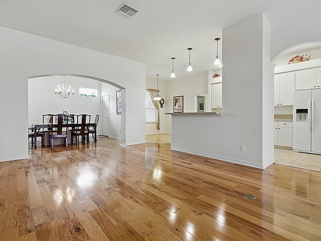 living room featuring arched walkways, light wood finished floors, a chandelier, and baseboards