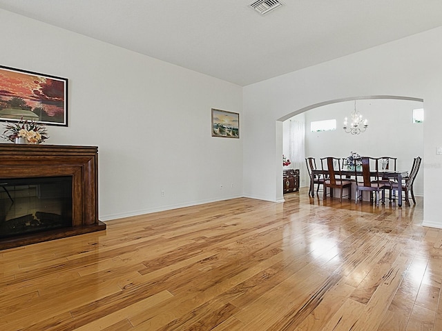 living room with arched walkways, light wood-type flooring, a chandelier, and baseboards