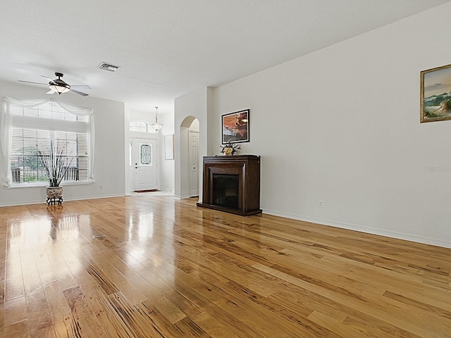 unfurnished living room with arched walkways, ceiling fan, light wood-style floors, a fireplace, and baseboards
