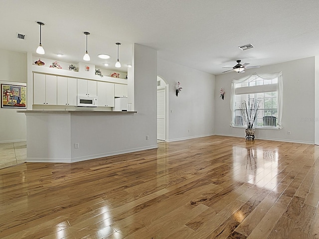 unfurnished living room featuring light wood-style flooring, ceiling fan, arched walkways, and baseboards