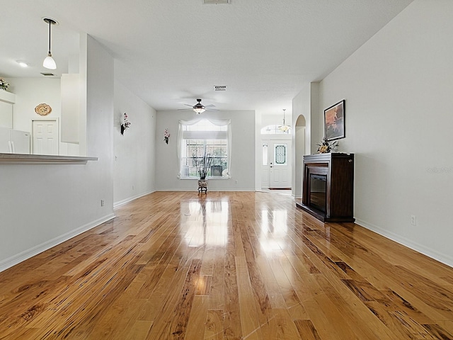 unfurnished living room with hardwood / wood-style flooring, arched walkways, a ceiling fan, and baseboards