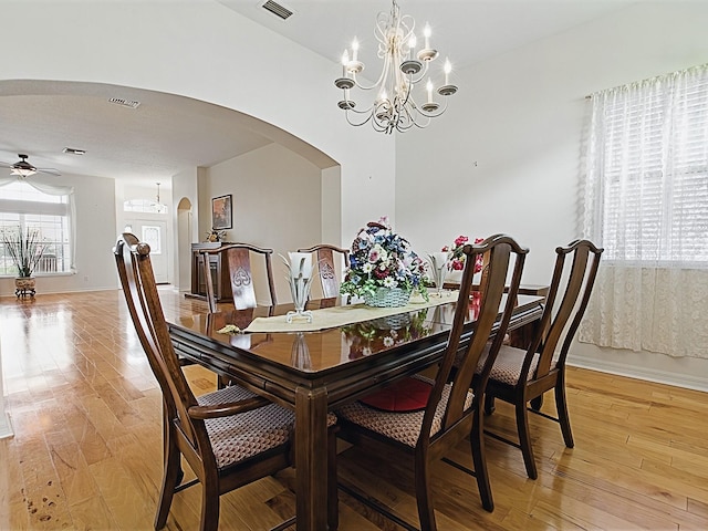 dining area featuring arched walkways, light wood-style floors, a chandelier, baseboards, and ceiling fan