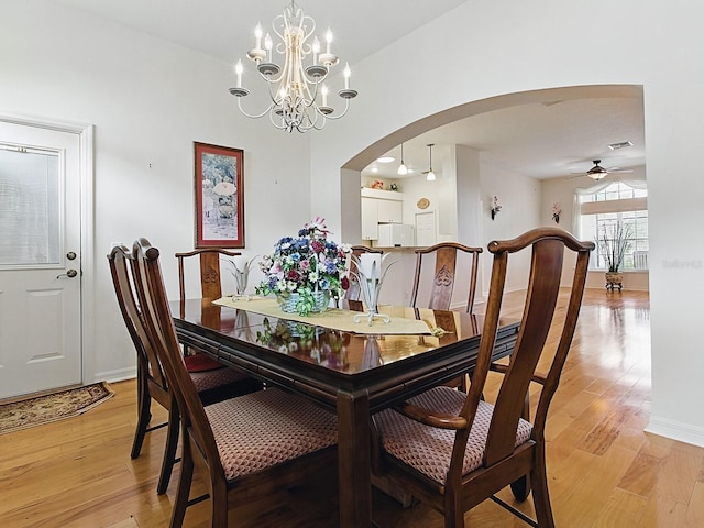 dining space with arched walkways, light wood-type flooring, a chandelier, and a ceiling fan