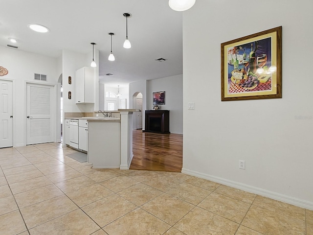 kitchen with arched walkways, light tile patterned flooring, white cabinetry, a peninsula, and pendant lighting