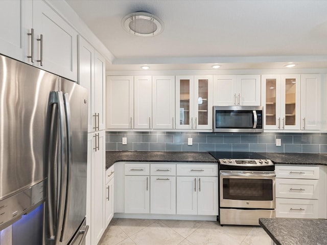 kitchen featuring appliances with stainless steel finishes, white cabinets, dark stone countertops, glass insert cabinets, and recessed lighting