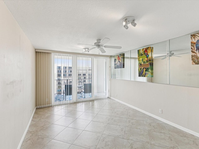 spare room with a ceiling fan, a textured ceiling, baseboards, and floor to ceiling windows