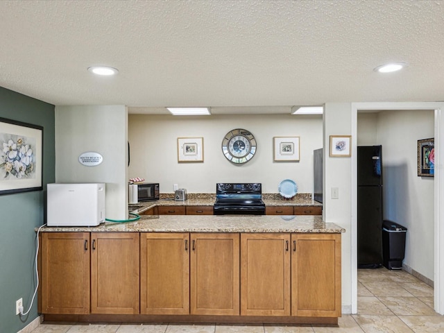 kitchen with black appliances, brown cabinets, a peninsula, light stone counters, and a textured ceiling