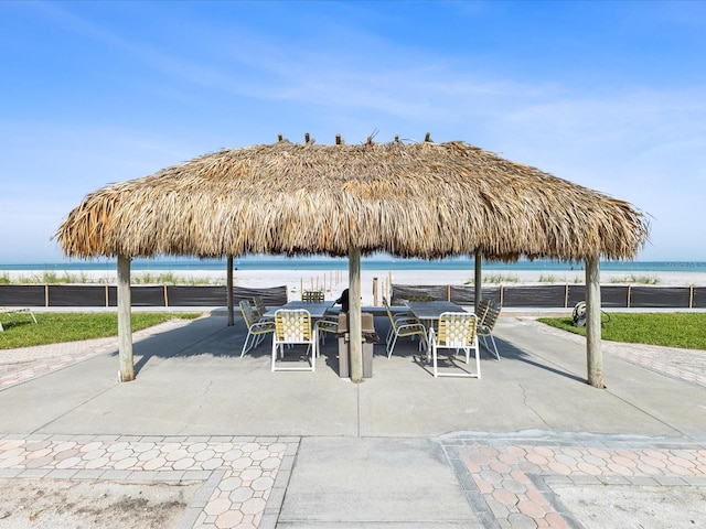 view of patio featuring outdoor dining area, view of water and beach, and fence