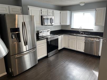 3041 Bloomsbury Dr, Kissimmee, FL 34747 - kitchen with stainless steel appliances, a sink, dark countertops, white cabinets, and a textured ceiling