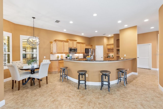 1123 Barnacle Ter, The Villages, FL 32162 - kitchen featuring stainless steel appliances, light brown cabinetry, a chandelier, a breakfast bar, and baseboards