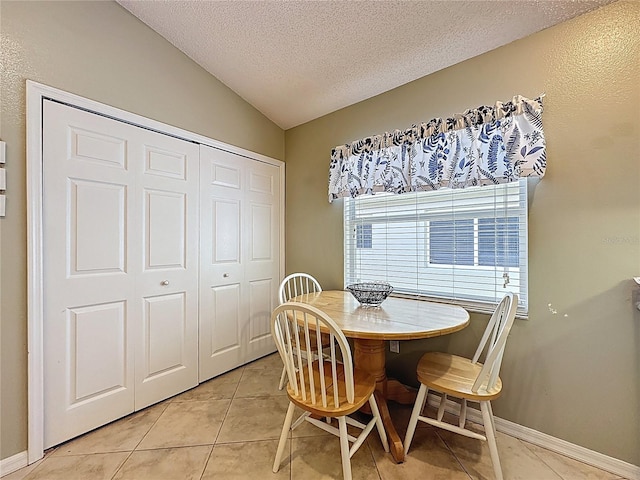 dining room with a textured ceiling, light tile patterned floors, and vaulted ceiling