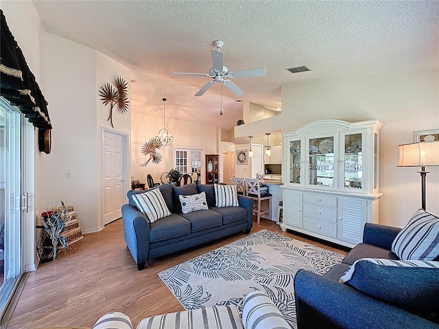 living area featuring a ceiling fan, vaulted ceiling, light wood-style flooring, and a textured ceiling