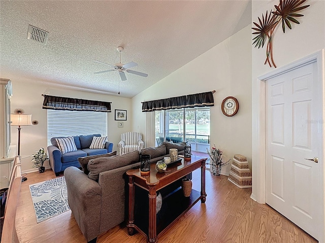 living room with a ceiling fan, light wood-type flooring, vaulted ceiling, a textured ceiling, and baseboards
