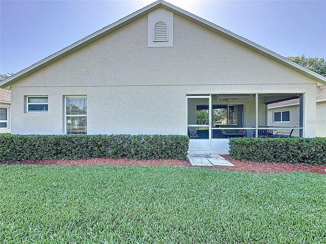 rear view of house with a yard, a sunroom, and stucco siding