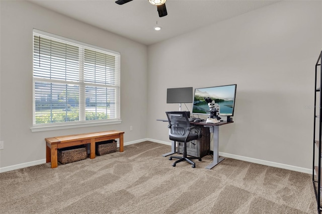 carpeted office space featuring a ceiling fan and baseboards