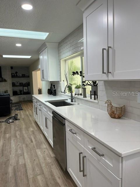 kitchen with a sink, black dishwasher, light wood-type flooring, white cabinets, and recessed lighting