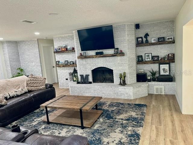 living area featuring wood finished floors, a textured ceiling, a brick fireplace, and recessed lighting