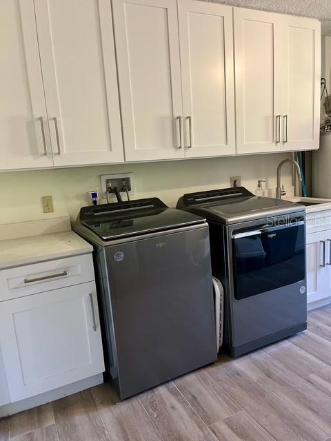 laundry area featuring independent washer and dryer, cabinet space, and light wood-style floors