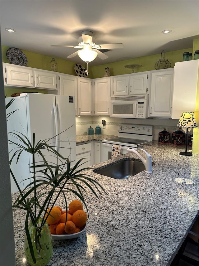 kitchen with white appliances, light stone counters, a sink, white cabinets, and recessed lighting