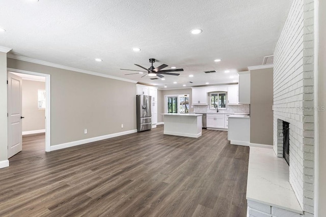 unfurnished living room featuring crown molding, a ceiling fan, recessed lighting, a brick fireplace, and baseboards