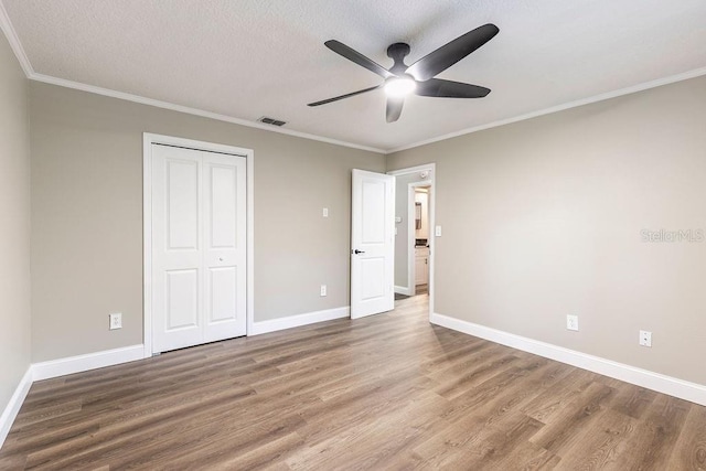 unfurnished bedroom with wood finished floors, a closet, baseboards, ornamental molding, and ceiling fan
