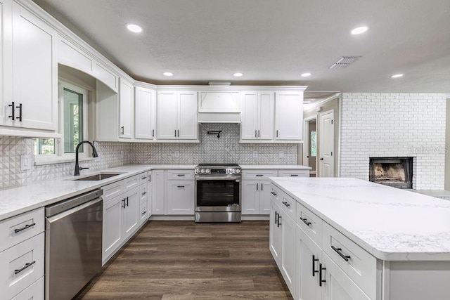 kitchen with stainless steel appliances, a sink, a brick fireplace, plenty of natural light, and recessed lighting