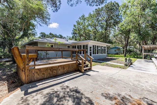 rear view of house with a sunroom, a deck, and a patio