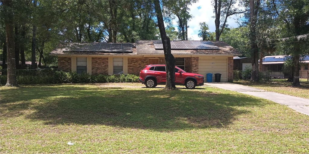 11820 N Par Ter, Dunnellon, FL 34434 - ranch-style house featuring brick siding, solar panels, a front yard, and an attached garage