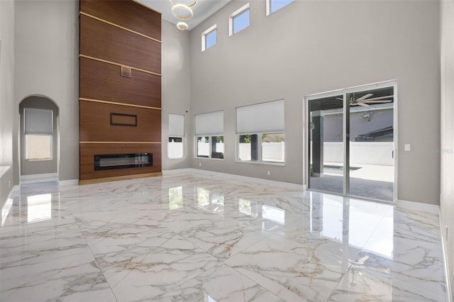 unfurnished living room featuring marble tiled floors, a high ceiling, a glass covered fireplace, baseboards, and arched walkways
