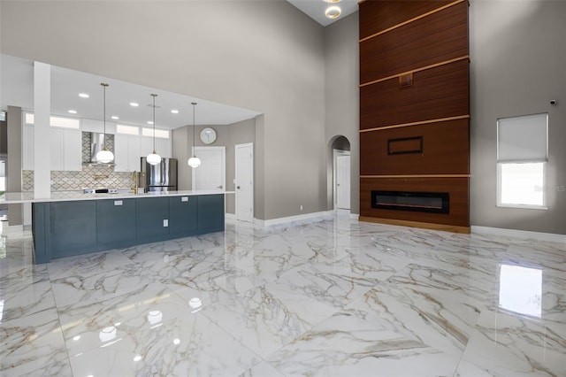 unfurnished living room featuring a towering ceiling, light marble finish flooring, baseboards, arched walkways, and a large fireplace
