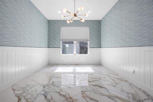 empty room with a chandelier, a wainscoted wall, and marble finish flooring