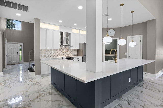 kitchen with wall chimney exhaust hood, light marble finish floors, stainless steel appliances, baseboards, and white cabinetry