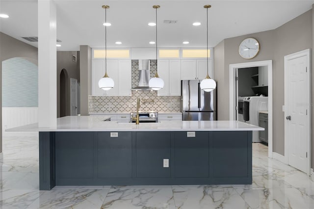 kitchen featuring appliances with stainless steel finishes, wall chimney range hood, light marble finish floors, arched walkways, and white cabinetry