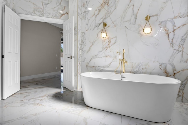 bathroom with marble tiled floors, stone wall, and a soaking tub