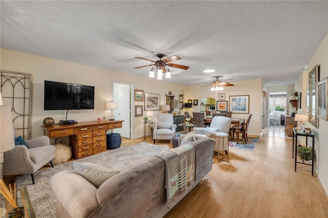 living room with ceiling fan, light wood-style flooring, a textured ceiling, and baseboards