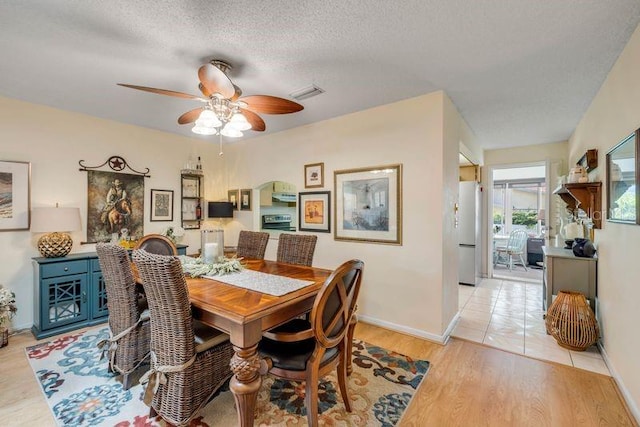 dining room featuring a textured ceiling, a ceiling fan, light wood finished floors, and baseboards