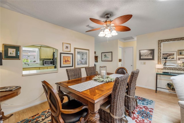 dining space with ceiling fan, light wood-style floors, baseboards, and a textured ceiling