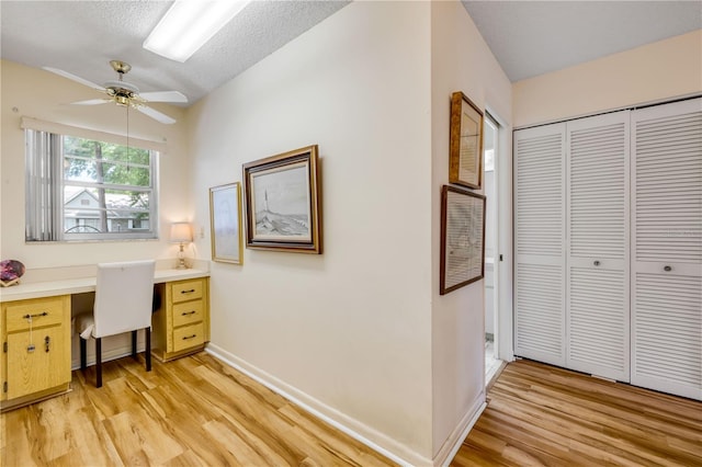 office with light wood-style flooring, a ceiling fan, baseboards, and built in desk