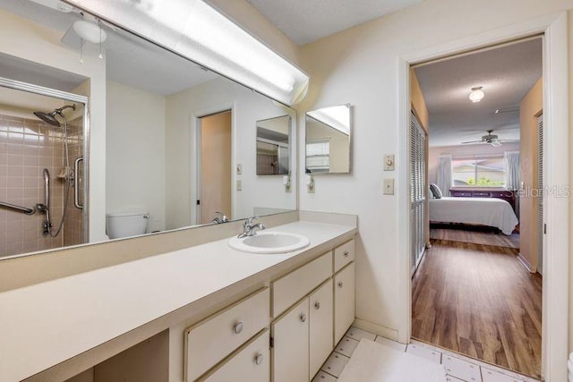 ensuite bathroom featuring ceiling fan, toilet, tiled shower, baseboards, and vanity
