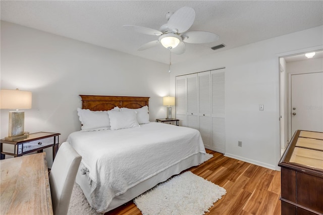 bedroom with a closet, light wood-style flooring, baseboards, a ceiling fan, and a textured ceiling