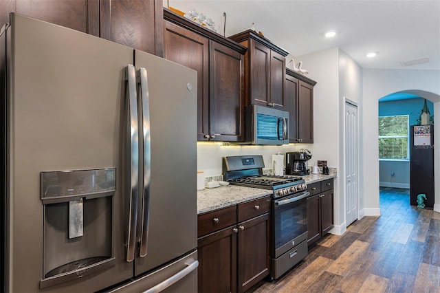 4581 Shenandoah River Trl, Leesburg, FL 34748 - kitchen with stainless steel appliances, arched walkways, dark brown cabinetry, dark wood finished floors, and baseboards