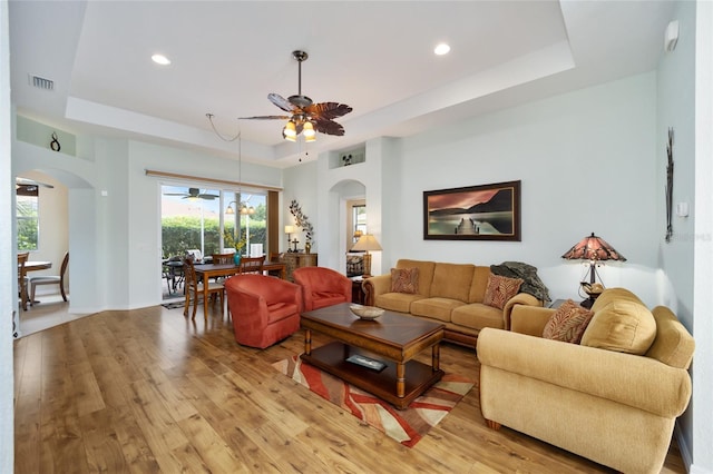 living area with arched walkways, a tray ceiling, ceiling fan, light wood-type flooring, and recessed lighting